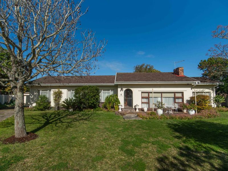 A well-maintained single-story residential home featuring a tiled roof, brick chimney, and a spacious front garden with a paved walkway and driveway.