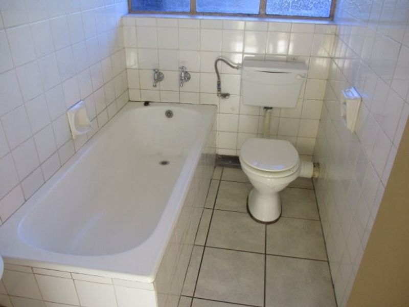A compact, dated bathroom featuring a standard bathtub, toilet, and full-height ceramic wall tiling.