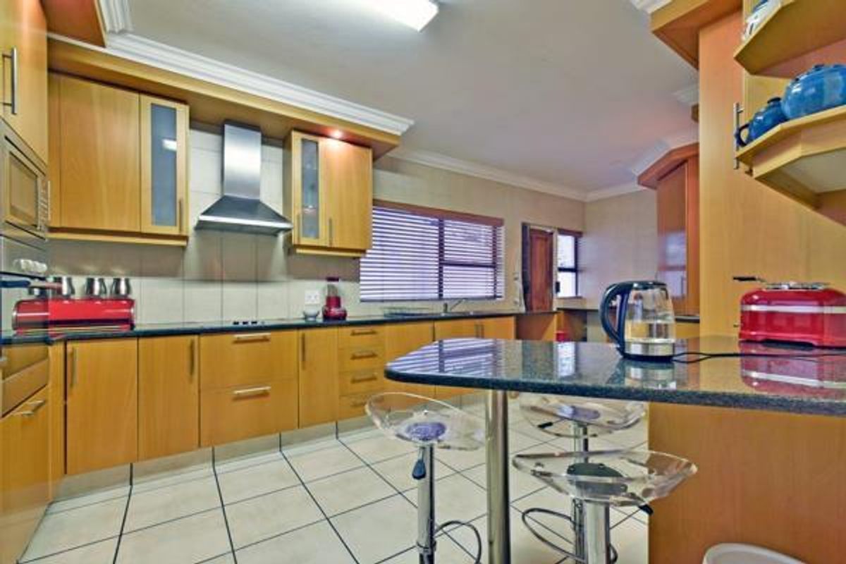 A functional kitchen featuring light wood cabinetry, dark granite countertops, a stainless steel extractor fan, and tiled flooring with a breakfast bar area.