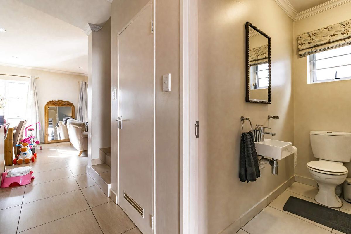 A compact guest bathroom featuring a wall-mounted basin and toilet, adjacent to a tiled hallway area.