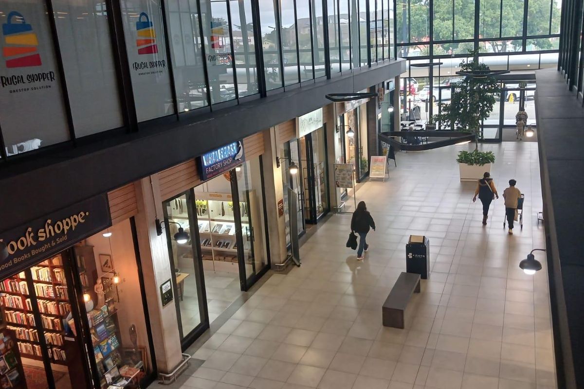 A modern indoor retail walkway featuring glass storefronts, tiled flooring, and high ceilings with natural light, providing a clean and professional shopping environment.
