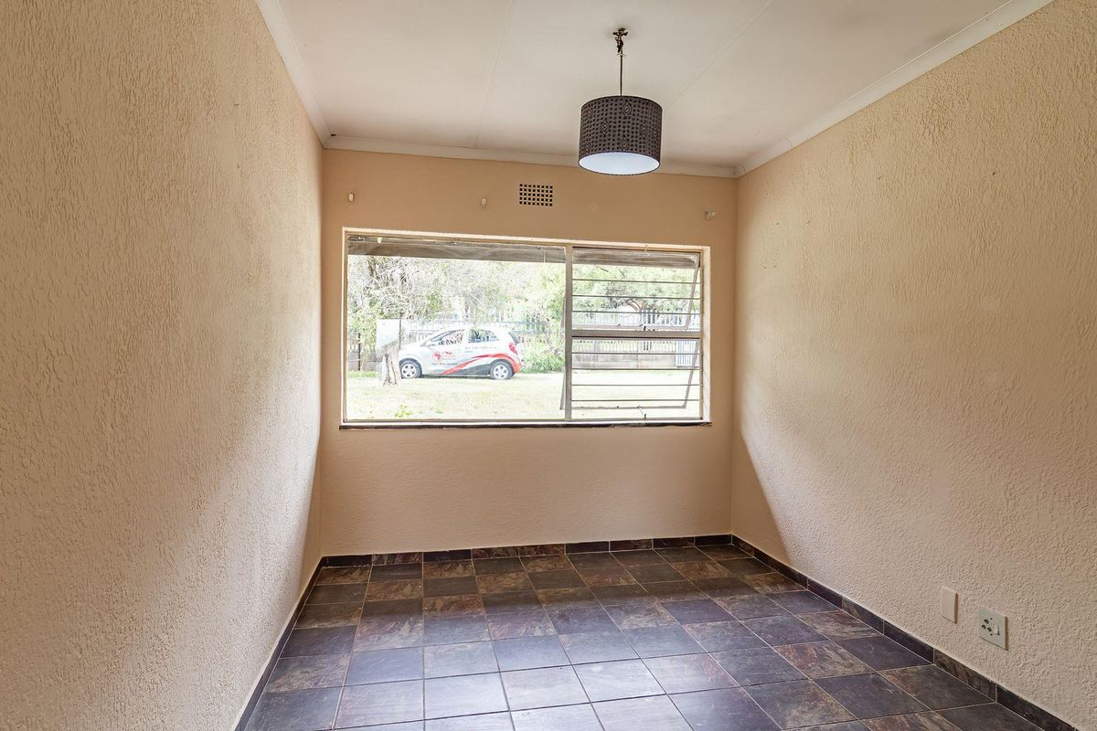 A simple, empty room featuring tiled flooring, textured walls, and a large window providing natural light and a view of the exterior.