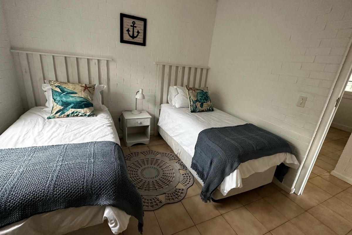 A bedroom featuring white painted brick walls and tiled flooring, configured with two single beds.