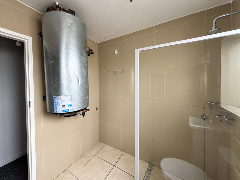 Bathroom featuring a glass shower enclosure, pedestal sink, toilet, and a wall-mounted electric water heater with exposed plumbing.