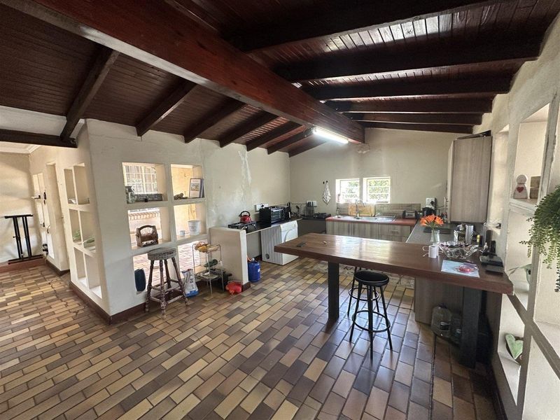 Open plan kitchen and living area featuring exposed timber beams, terracotta tile flooring, and a breakfast bar with built-in cabinetry.
