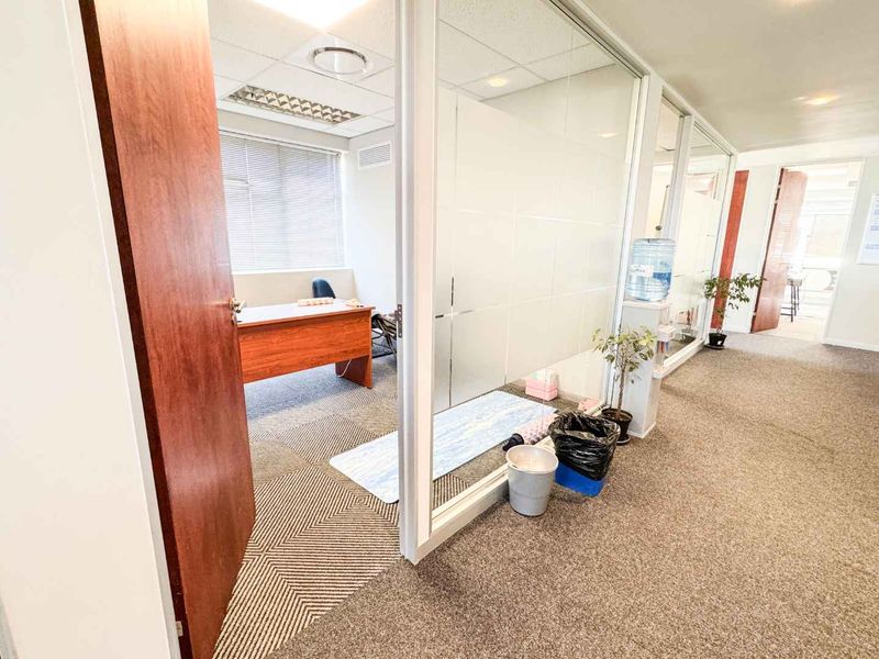 A professional office space featuring glass partition walls, carpeted flooring, and a suspended ceiling with recessed lighting, providing a functional workspace environment.