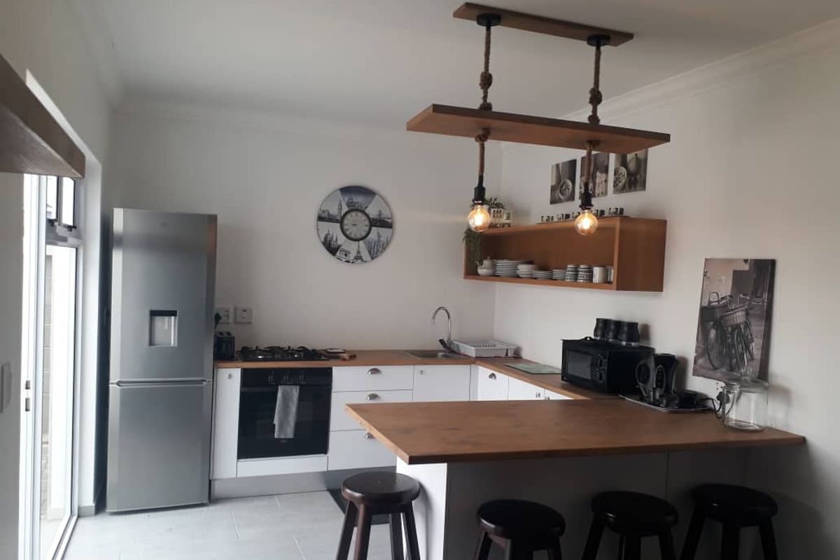 Modern kitchen featuring white cabinetry, wooden countertops, a built-in oven with gas hob, and a breakfast bar with pendant lighting.