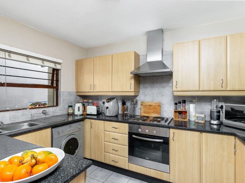 Functional kitchen featuring light wood cabinetry, granite countertops, built-in oven, electric hob, stainless steel extractor fan, and tiled finishes.