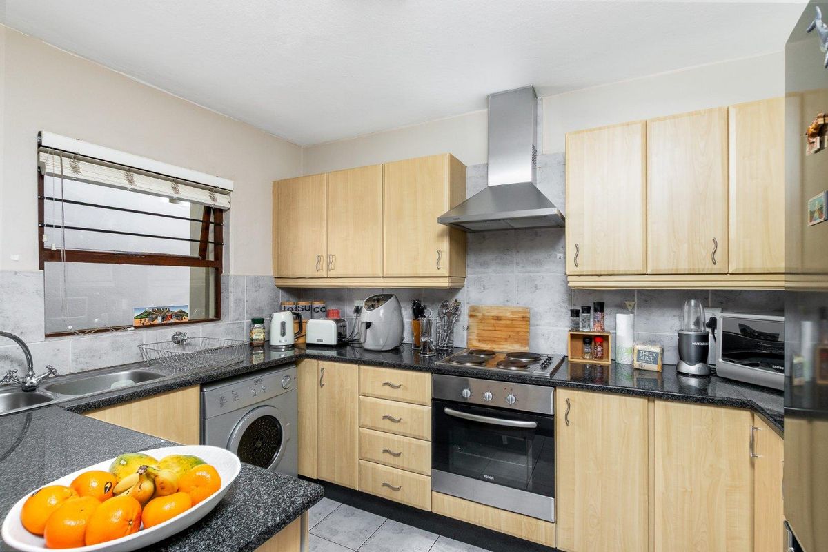 Functional kitchen featuring light wood cabinetry, granite countertops, built-in oven, electric hob, stainless steel extractor fan, and tiled finishes.