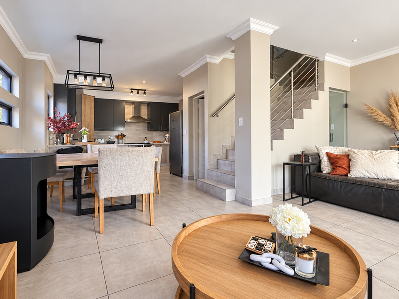 Spacious open-plan living and dining area featuring modern kitchen cabinetry, tiled floors, and a staircase with a contemporary metal railing.