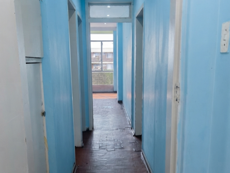 A functional hallway featuring parquet flooring and access to multiple rooms, leading towards an exterior balcony area.