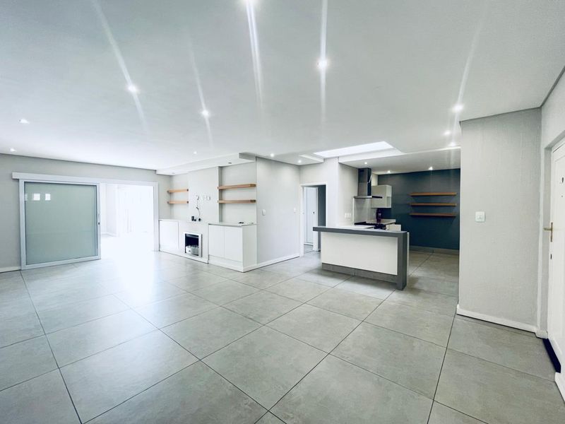 Spacious open-plan living and kitchen area featuring large format floor tiles, modern recessed lighting, a built-in fireplace, and a functional kitchen island.