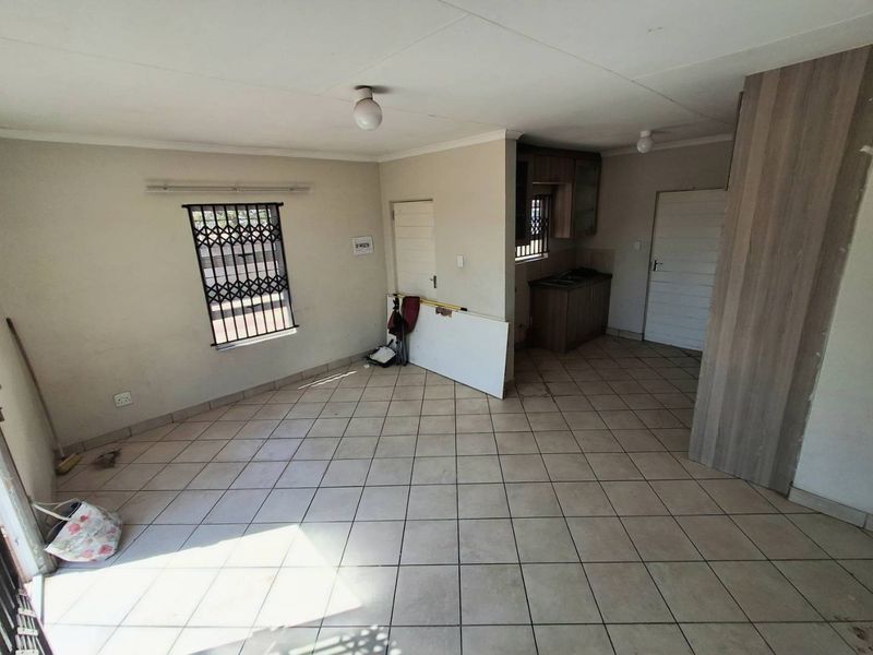 An open-plan living area featuring tiled flooring, a security gate on the window, and a compact kitchen with built-in cabinetry.