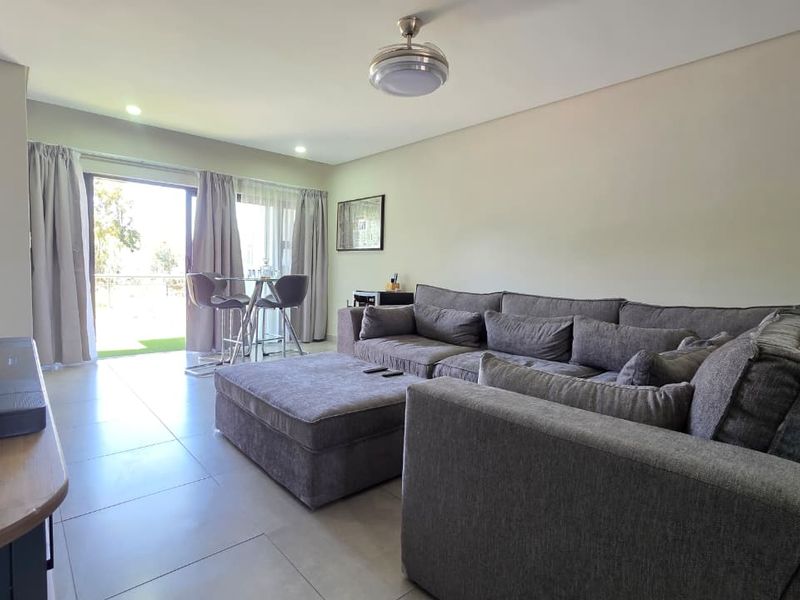 A well-maintained living room featuring neutral tiled flooring, recessed lighting, and a sliding glass door providing access to an outdoor area.