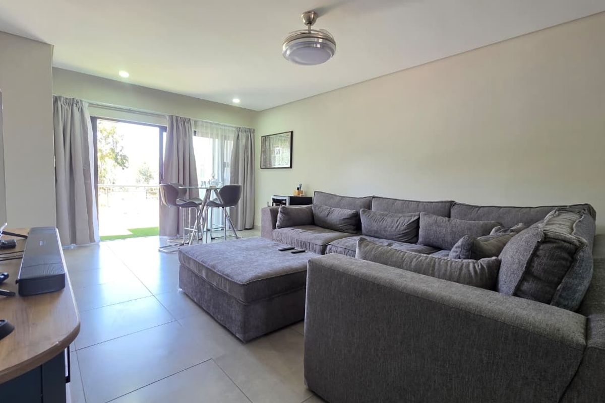 A well-maintained living room featuring neutral tiled flooring, recessed lighting, and a sliding glass door providing access to an outdoor area.