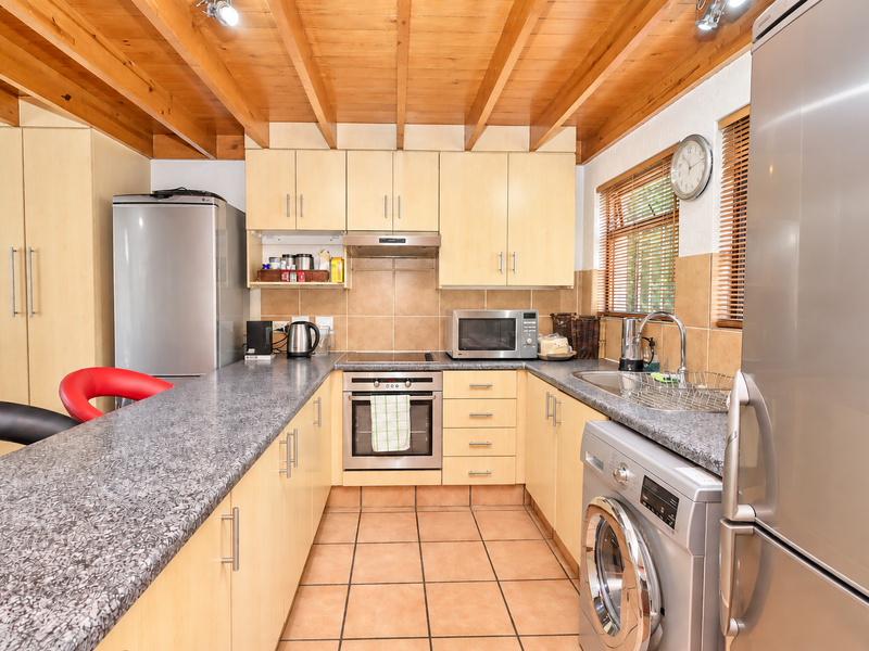 Functional kitchen featuring light wood cabinetry, laminate countertops, tiled flooring, and exposed timber beam ceiling with integrated stainless steel appliances.