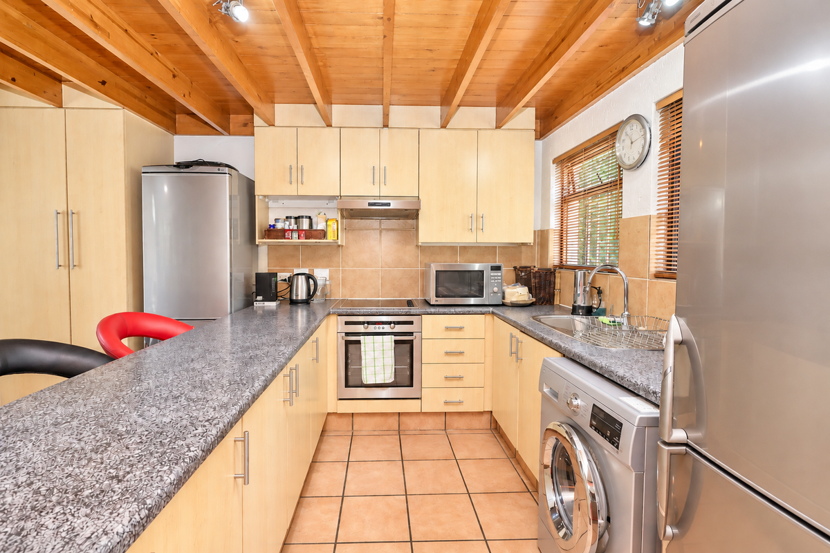 Functional kitchen featuring light wood cabinetry, laminate countertops, tiled flooring, and exposed timber beam ceiling with integrated stainless steel appliances.