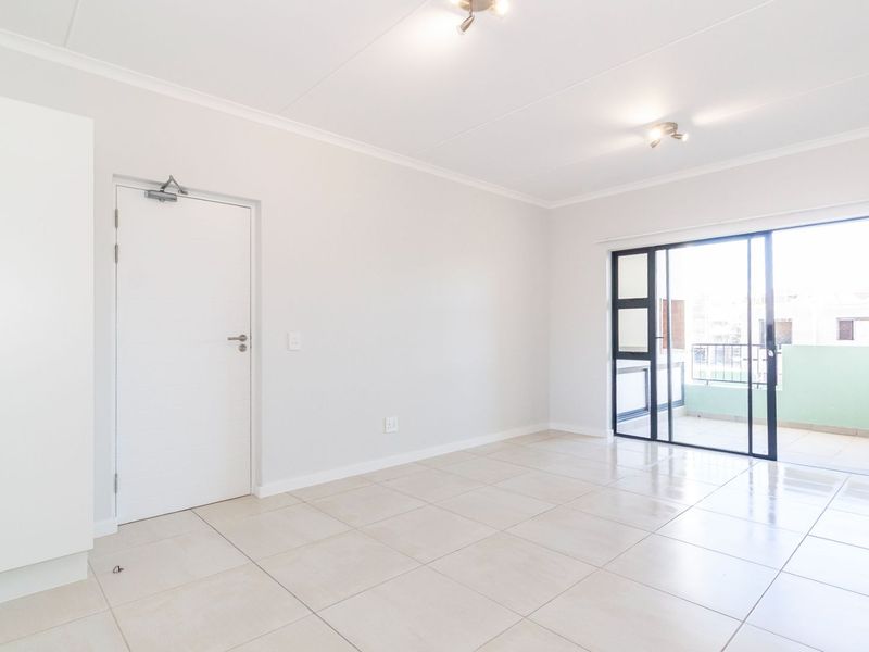 Bright and spacious open-plan living area featuring neutral tiled flooring, a built-in cupboard, and direct access to a private balcony through sliding glass doors.