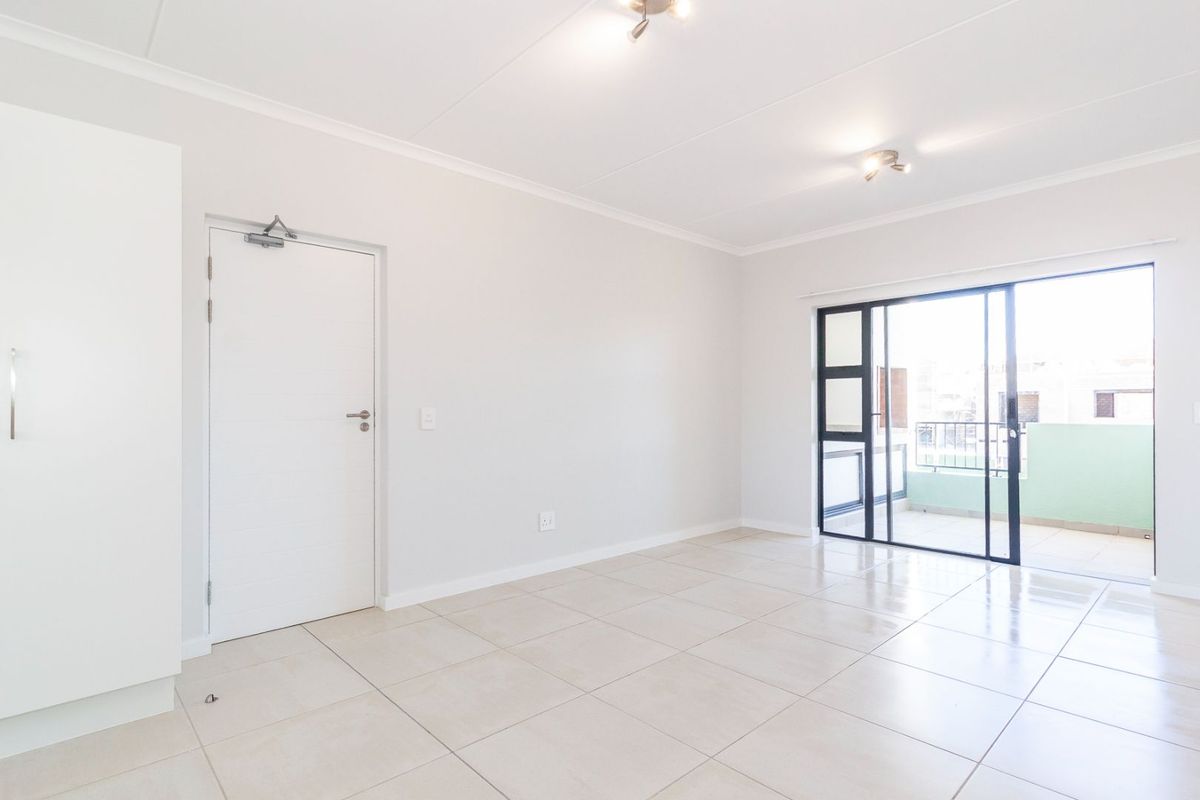 Bright and spacious open-plan living area featuring neutral tiled flooring, a built-in cupboard, and direct access to a private balcony through sliding glass doors.