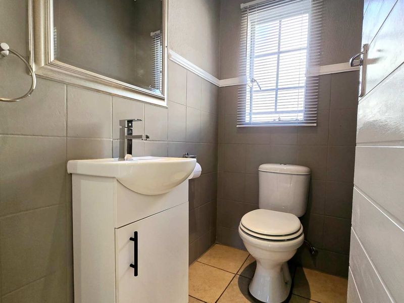 A compact, well-maintained bathroom featuring a modern vanity, basin, toilet, and neutral wall tiling with a window for natural light.