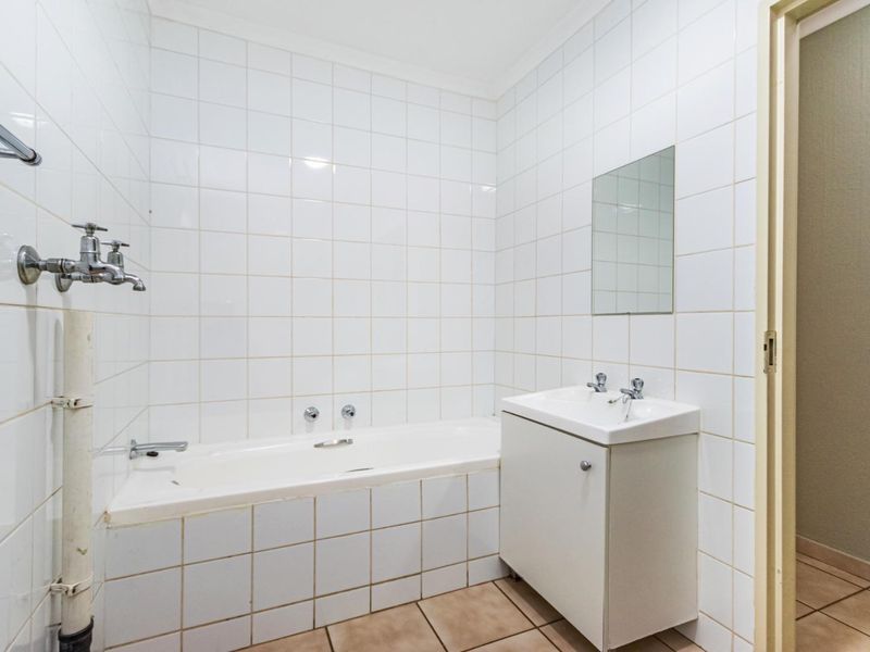 A functional bathroom featuring a built-in bathtub, vanity cabinet, and wall-mounted mirror, finished with white wall tiles and neutral floor tiles.