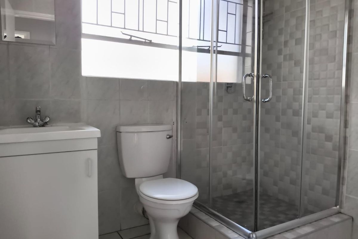 A functional bathroom featuring a vanity basin, a standard toilet, and a glass-enclosed shower with tiled finishes throughout.