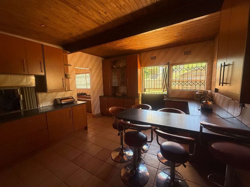 A functional kitchen featuring wooden ceilings, built-in cabinetry, tiled flooring, and a breakfast bar, with security bars installed on the windows.