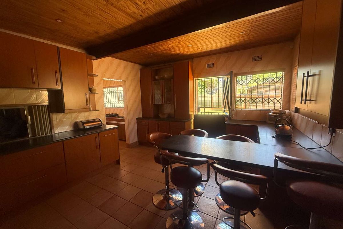 A functional kitchen featuring wooden ceilings, built-in cabinetry, tiled flooring, and a breakfast bar, with security bars installed on the windows.