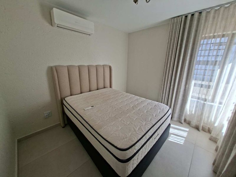 A well-maintained bedroom featuring tiled flooring, a wall-mounted air conditioning unit, and floor-to-ceiling curtains.