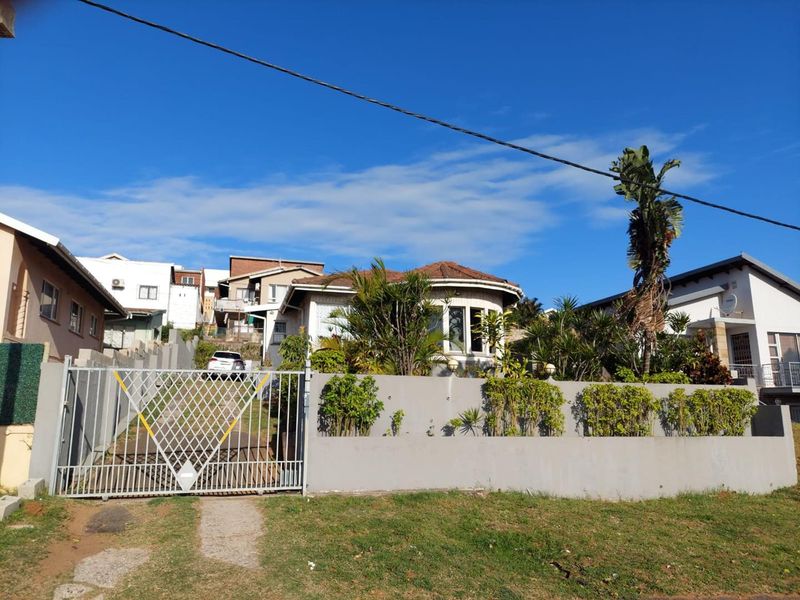 Front elevation of a residential house featuring a concrete boundary wall, metal driveway gate, and a prominent bay window.