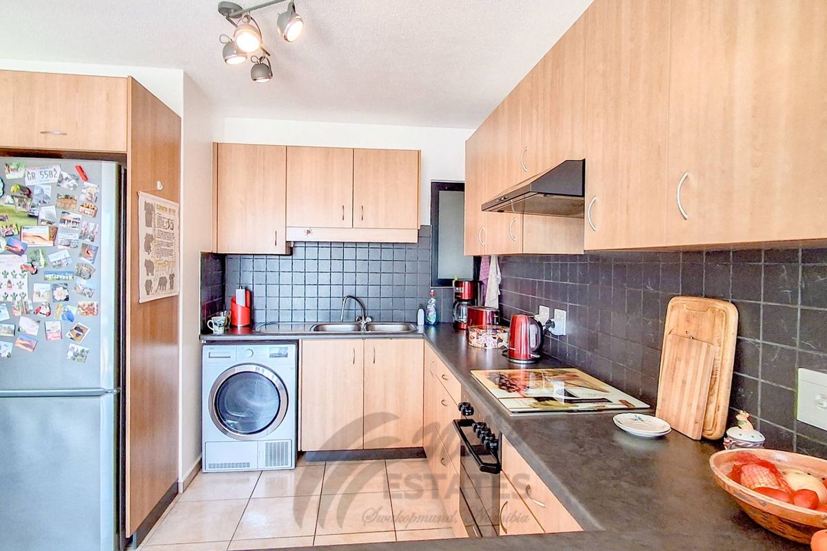 A functional kitchen featuring light wood cabinetry, dark tiled splashbacks, a built-in oven, extractor fan, and space for a washing machine.