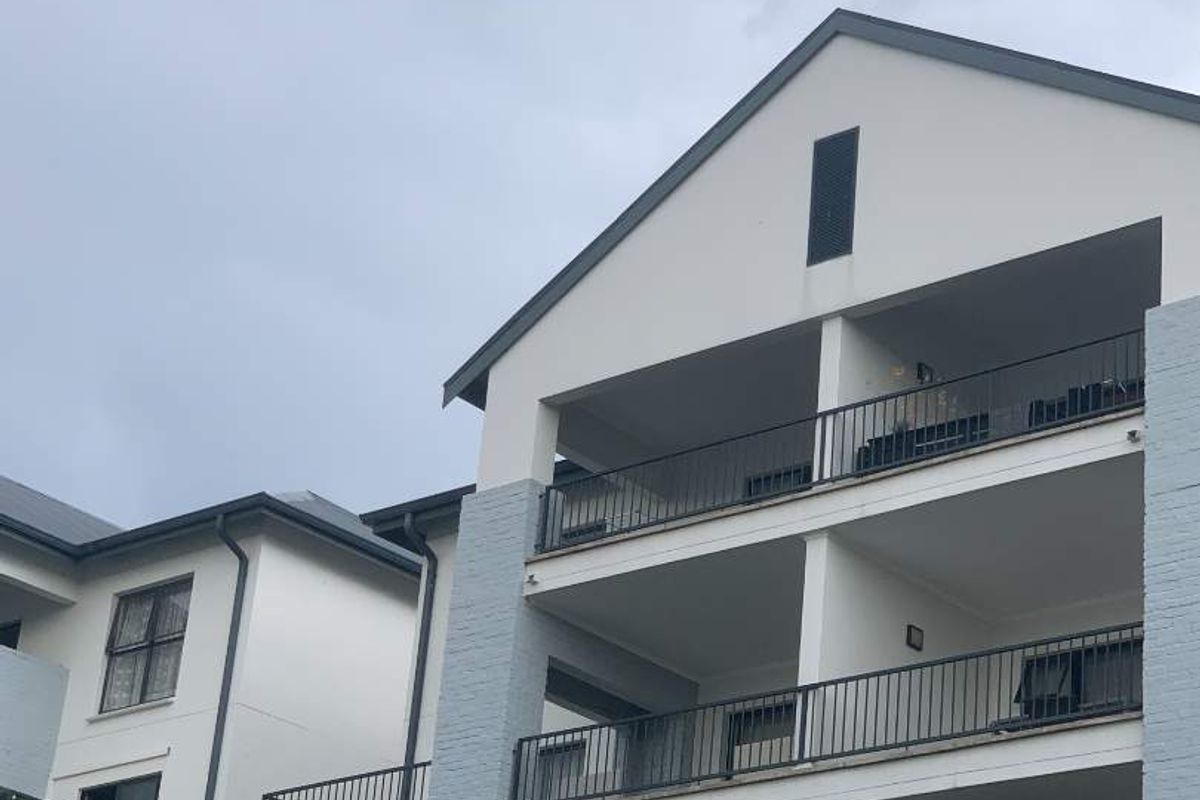 Exterior view of a multi-story apartment building featuring stacked balconies with metal railings and a pitched roof design.