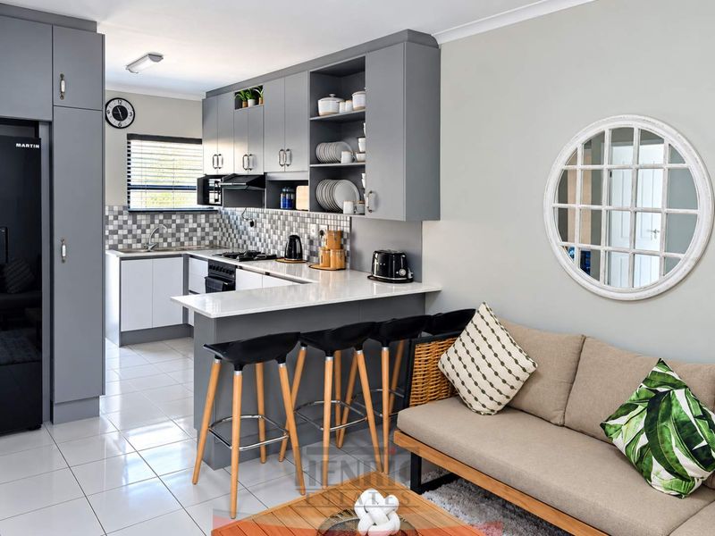 Modern open-plan kitchen featuring grey cabinetry, quartz countertops, gas hob, and a breakfast bar, seamlessly integrated with the living area.