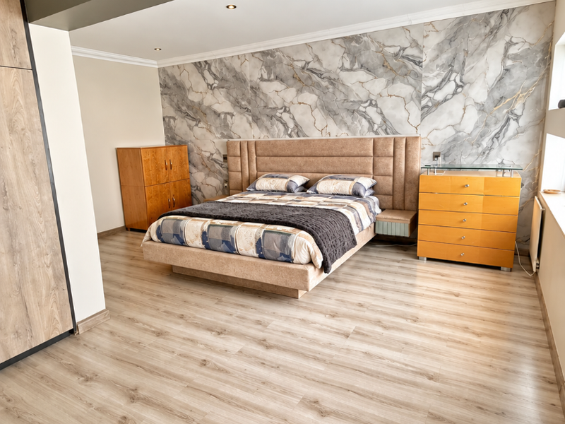 Spacious bedroom featuring modern laminate flooring, a striking marble-effect feature wall, recessed downlighting, and integrated wardrobe storage.