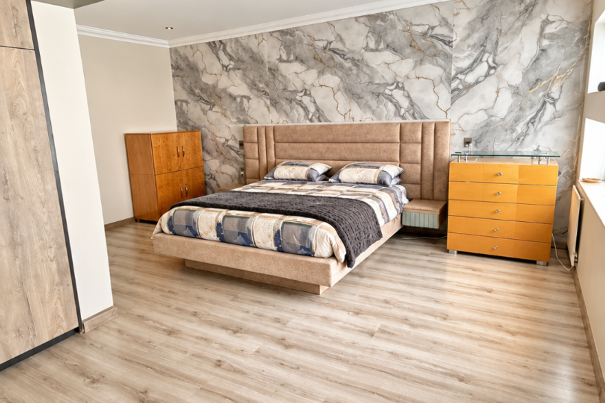Spacious bedroom featuring modern laminate flooring, a striking marble-effect feature wall, recessed downlighting, and integrated wardrobe storage.