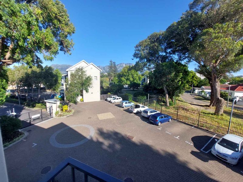 Elevated view overlooking the apartment complex parking area, surrounding trees, and distant mountain scenery.