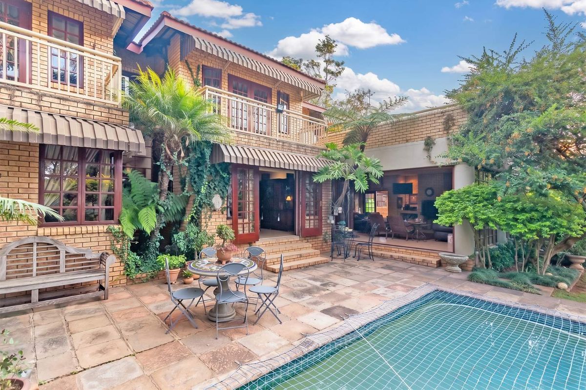 A spacious rear patio area featuring a swimming pool, brick facade, and direct access to the interior living spaces through large glass doors.