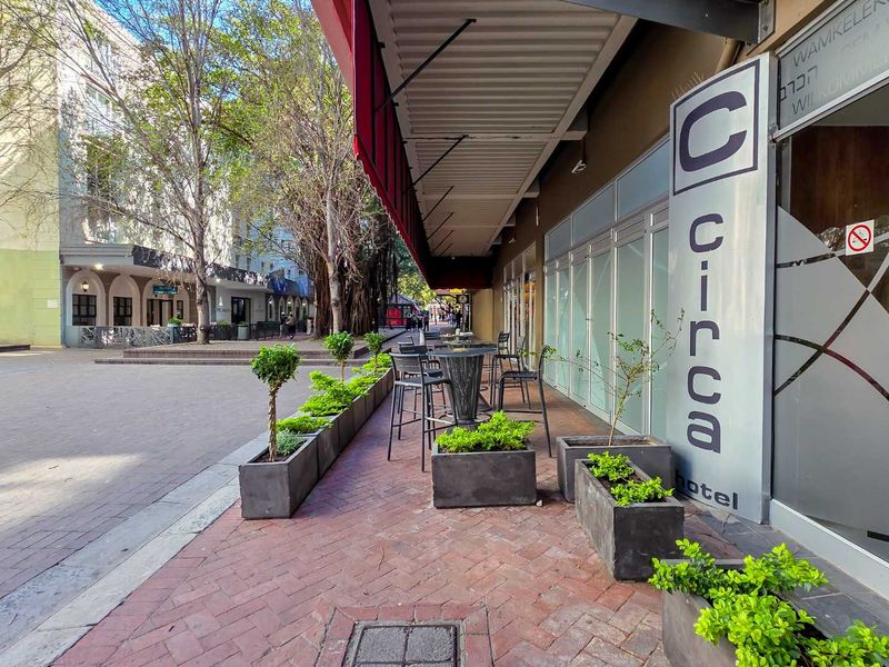 Outdoor seating area featuring a red awning, paved flooring, and modern glass facade entrance to the building.