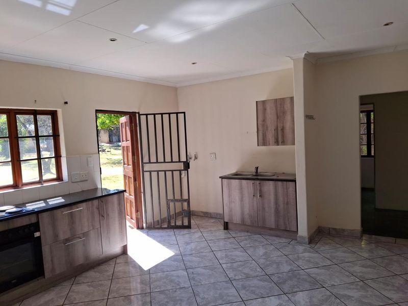 A bright, open-plan kitchen featuring modern wood-look cabinetry, dark laminate countertops, built-in oven, and tiled flooring with direct access to the exterior.
