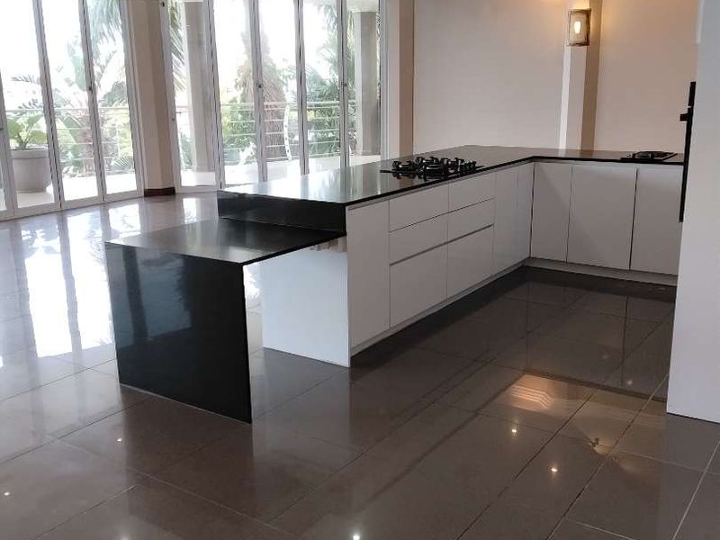 Modern open-plan kitchen featuring a sleek island with stone countertops, glossy cabinetry, and large floor-to-ceiling glass doors leading to an outdoor area.