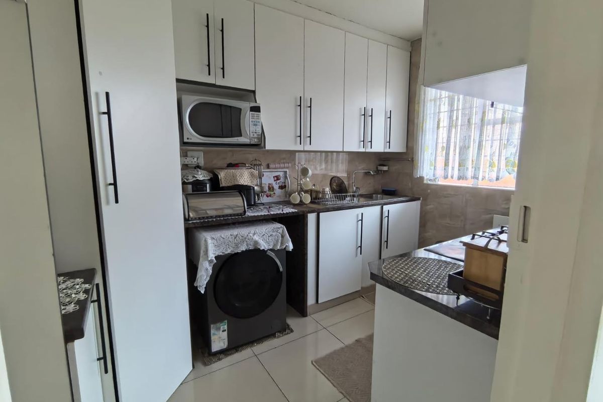 Compact kitchen featuring white cabinetry, dark countertops, tiled flooring, and integrated appliance space, offering a functional layout for apartment living.