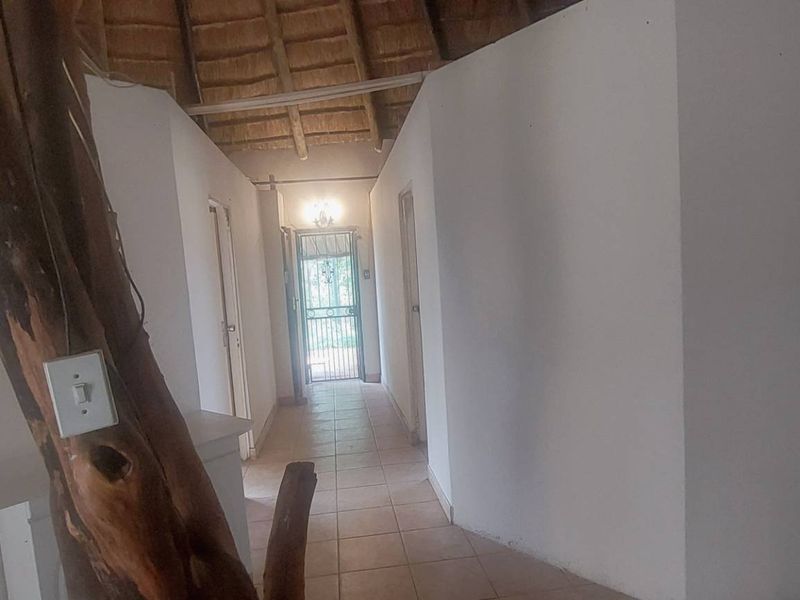 A rustic hallway featuring a traditional thatch roof, exposed timber support, and tiled flooring leading to a secure entrance.