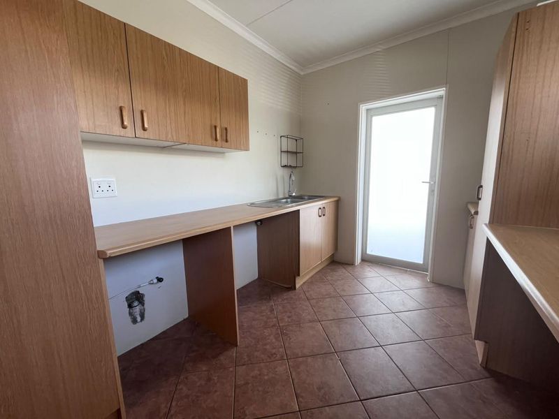 A functional laundry room featuring laminate cabinetry, a stainless steel sink, tiled flooring, and direct access to the exterior via a glass panel door.