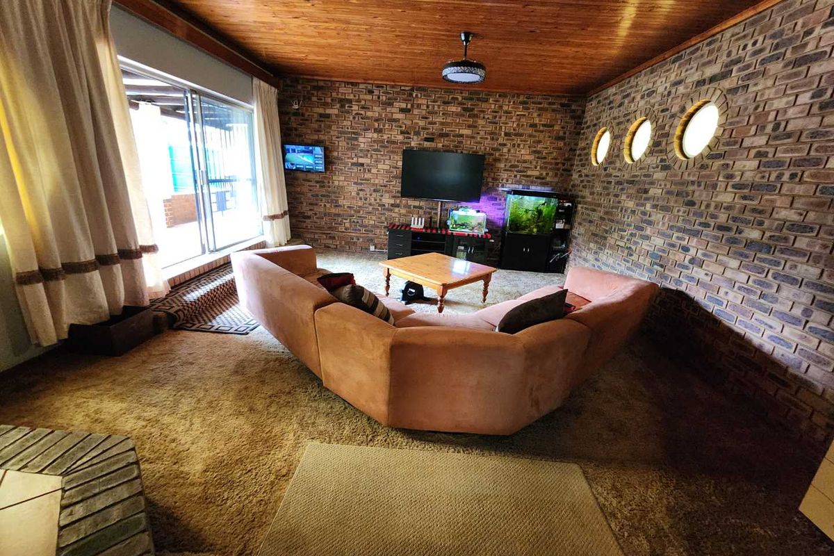 Spacious living room featuring exposed brick walls, unique circular accent windows, and a warm wood-paneled ceiling with direct access to the patio.
