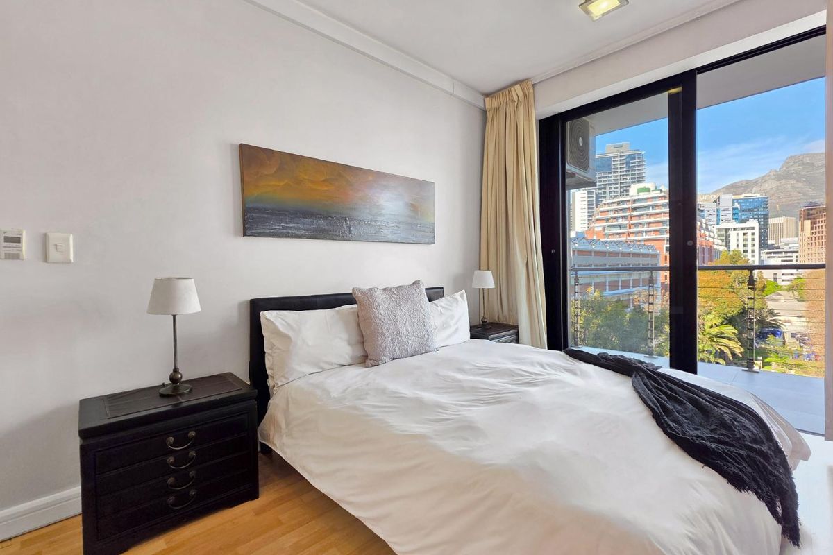 A bright bedroom featuring laminate flooring and a large sliding glass door that opens onto a private balcony with city views.