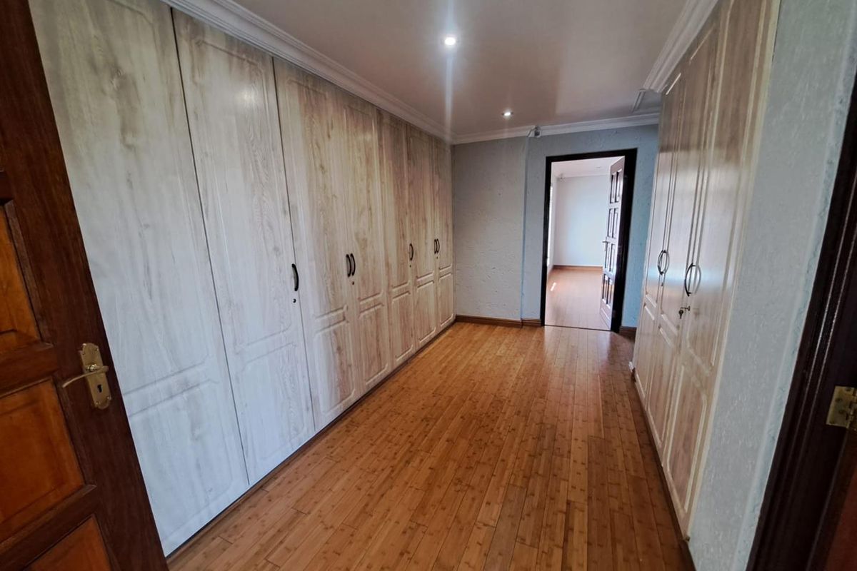 Spacious bedroom featuring extensive built-in cupboards, warm bamboo flooring, and modern recessed lighting, offering a clean and functional living space.