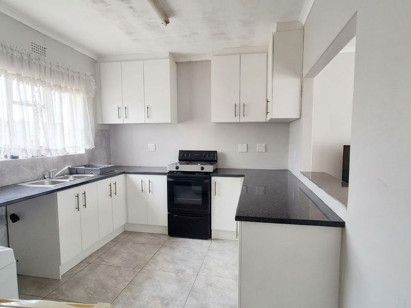 A functional kitchen featuring white cabinetry, dark laminate countertops, a freestanding stove, and tiled flooring with a convenient serving hatch to the adjacent room.