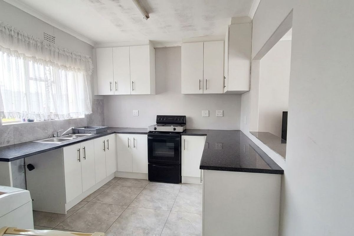 A functional kitchen featuring white cabinetry, dark laminate countertops, a freestanding stove, and tiled flooring with a convenient serving hatch to the adjacent room.