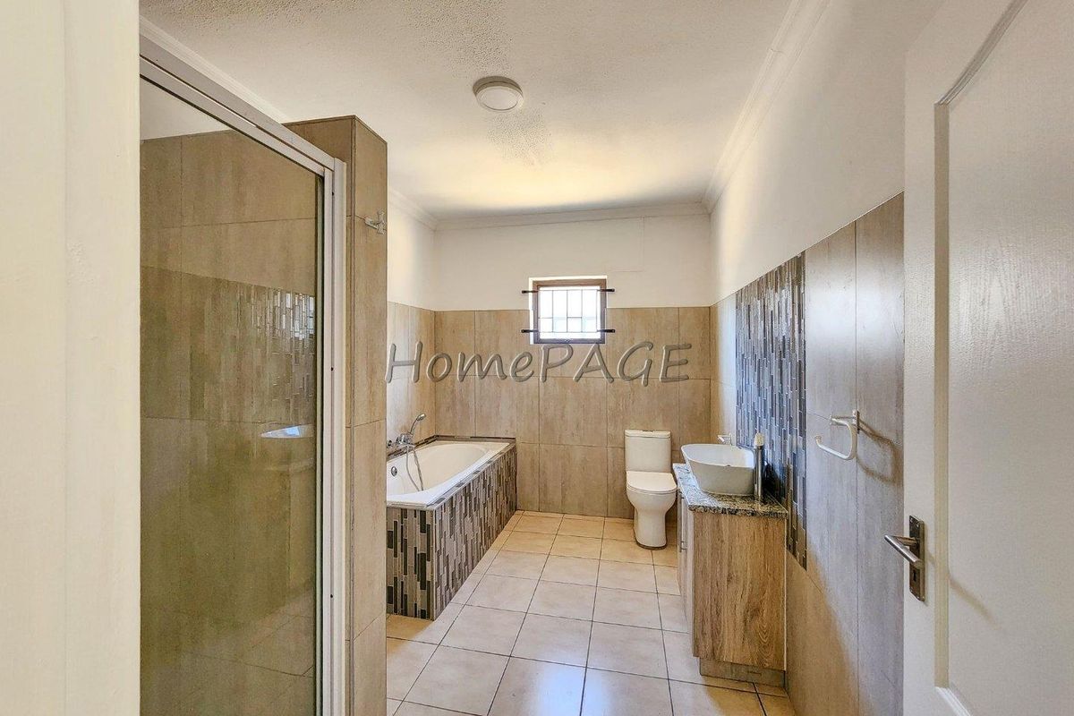 A clean, modern bathroom featuring a built-in bathtub, separate shower enclosure, vanity with vessel sink, and neutral tiled finishes throughout.