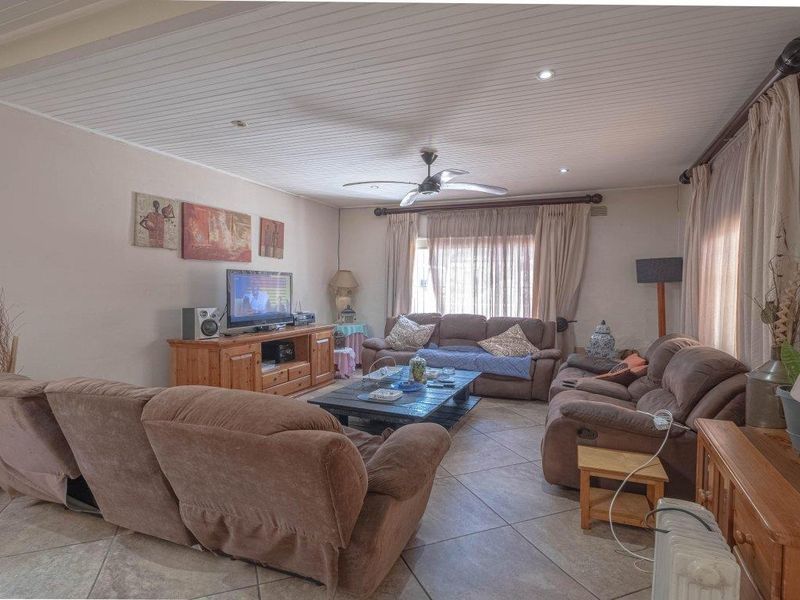 A spacious living room featuring tiled flooring, a tongue and groove ceiling with recessed lighting, and a central ceiling fan.